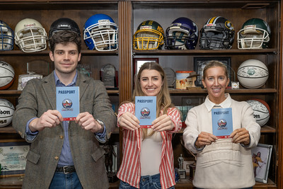 Three young people hold up passports while standing in front of football equipment.