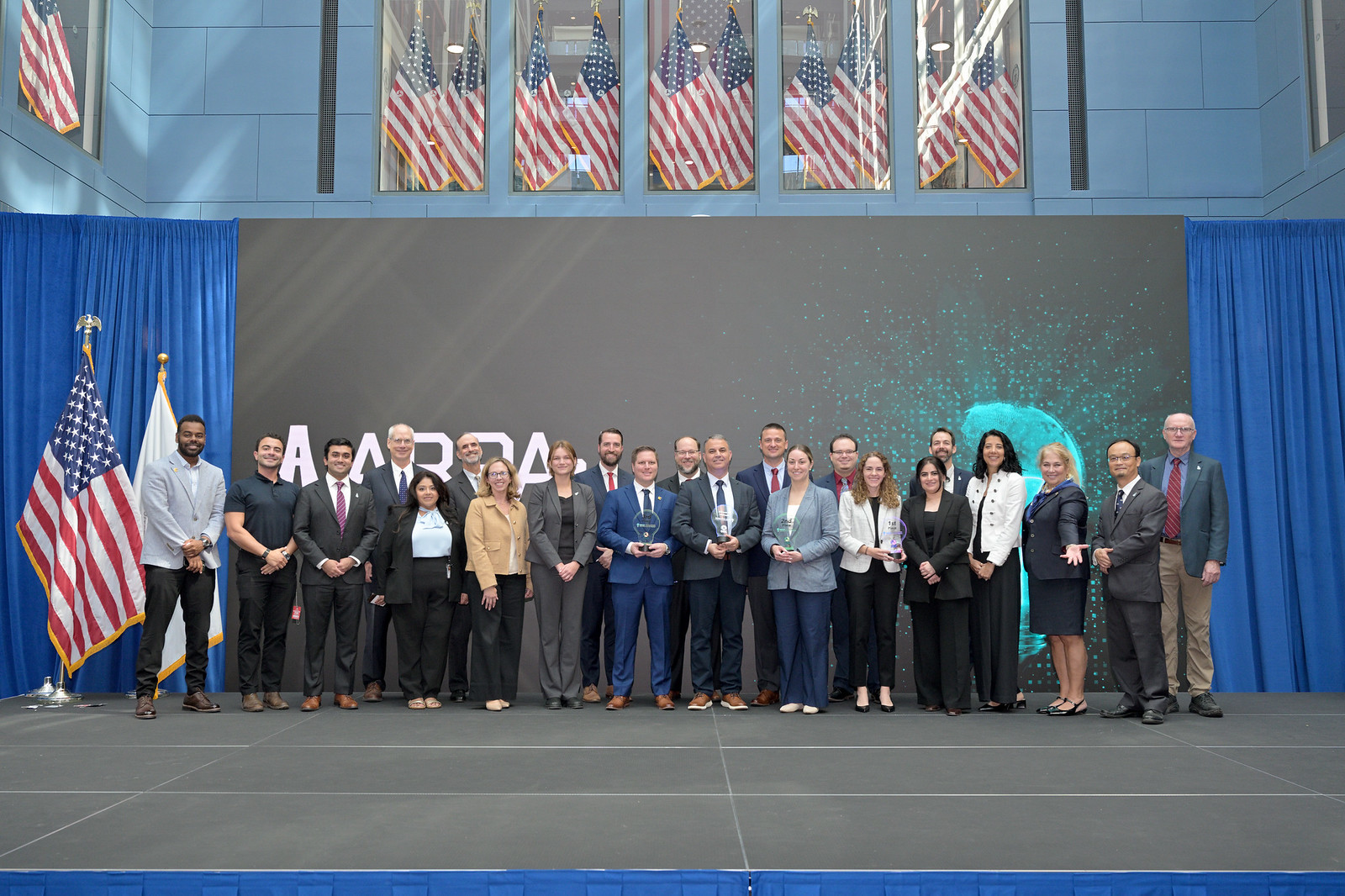 Ideas Challenge Finals attendees standing in front of an LED wall with a lightbulb animation at U.S. DOT Headquarters.