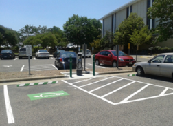 A charging station and dedicated parking space in a public parking lot. Other vehicles are picture in the background