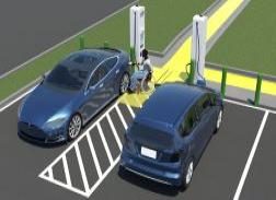 An overhead view of electric vehicles in dedicated parking spaces. A person is seated in a chair next to one of the cars as it charges.