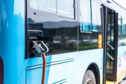 A charging cable is plugged into the side of a transit bus. The side doors of the bus are open.