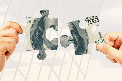 Two hands match up two puzzle pieces that, together, make up a $100 bill.