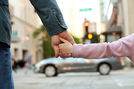 Child holding a parent's hand while standing at a traffic intersection.
