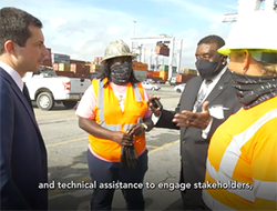USDOT Secretary Pete Buttigieg meets with stakeholders who are wearing hardhats and safety vests at a freight facility.