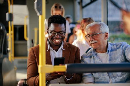 Two men sitting next to each other on a bus looking at a smartphone. 