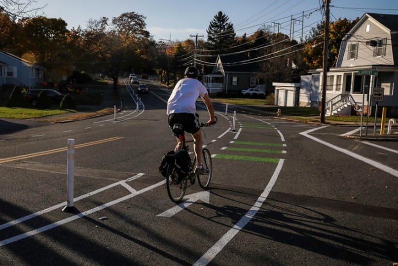 A picture showing a street with a person riding a bicycle in a bike lane separated by plastic delineators. It shows use of temporary materials to create separate bicycle infrastructure.
