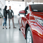 Two people stand examining a new vehicle on the showroom floor of a car dealership.