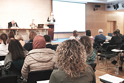 A diverse group of people listen to a panelist speaking at a community forum.
