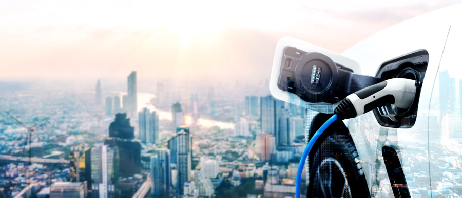 Close-up of a charging cable plugged into an electric vehicle. The image of the charging vehicle is overlaid on an aerial view of a city with skyscrapers. A river runs through the city.