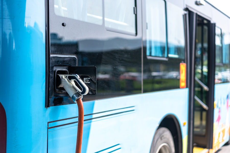A charger is plugged into the side of a transit bus.