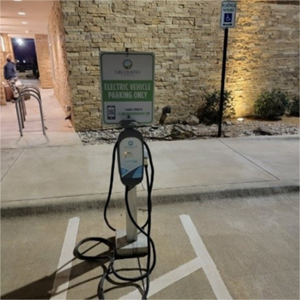 An EV charger with a long cord in a parking lot. The sign on the EV charger says, “Electric Vehicle Parking Only.”