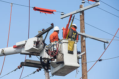 Two workers elevated in a cherry picker service the lines at the top of an electric utility pole.