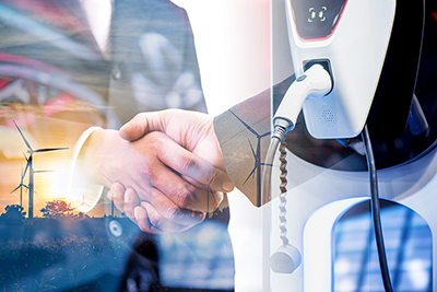 Two businesspeople shaking hands to indicate a partnership, superimposed over an image of an electric vehicle charger.
