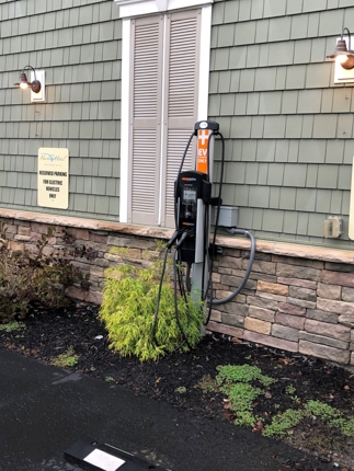 EV charger installed in a garden bed along the exterior edge of a building. A shrub is next to the charger.