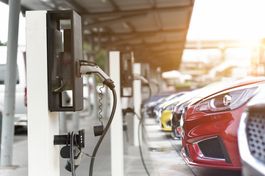 Side view of a row of cars parked in front of EV chargers.