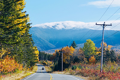 A truck travels down a two-lane road in a rural, mountainous area with trees and forest on both sides of the road.