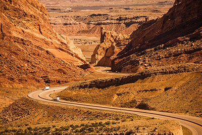 A freight truck travels through a desert canyon with high rocky hills on either side of the road. 