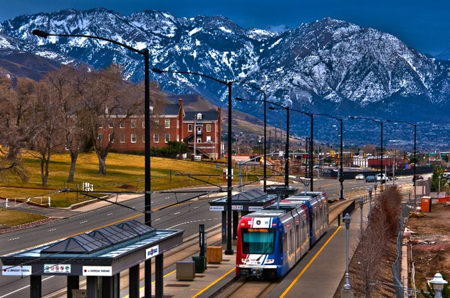 A Utah Transit Authority train pulls into a transit stop in a rural mountainous region.