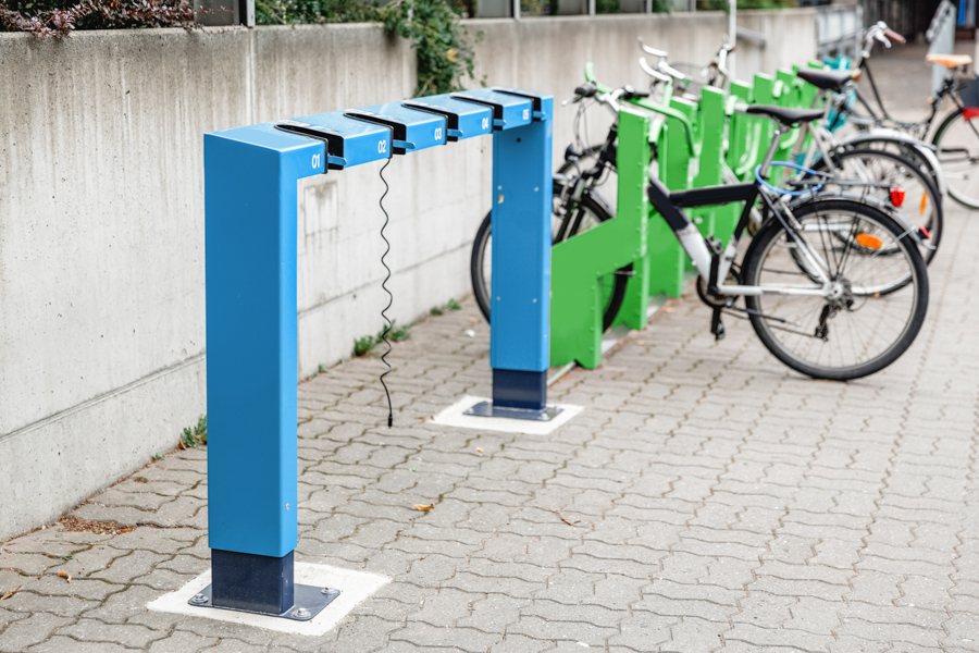 Electric bikes parked in a docking station on a brick sidewalk