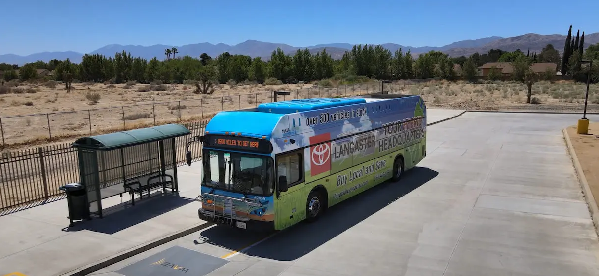 A transit bus next to a bus shelter. The bus is being charged by a charging pad on the pavement.