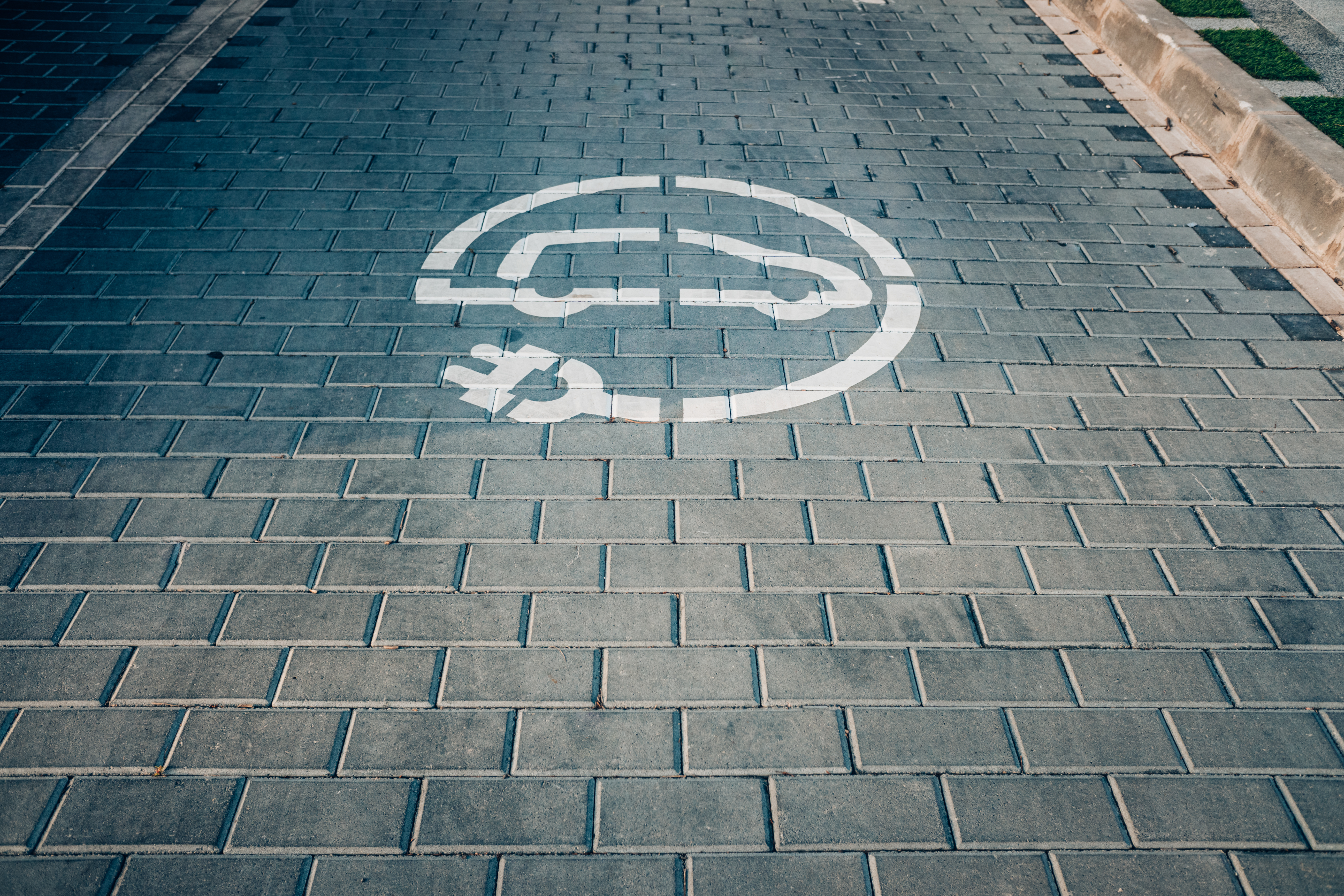 an EV charging symbol painted on a brick road. The symbol is the outline of a vehicle with an attached plug.