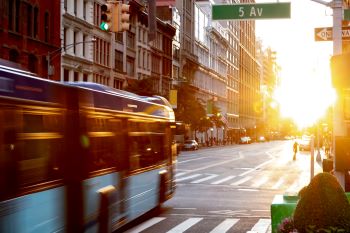 New York City street with bus passing through intersection at sunset.