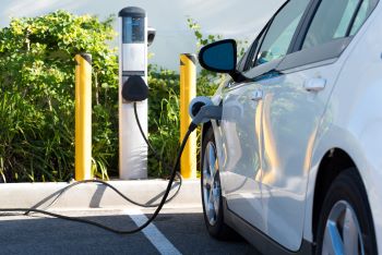 Electric vehicle plugged into charger in a parking spot.