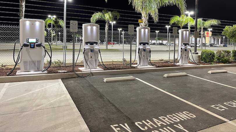 A row of four DC fast chargers next to empty parking spaces.