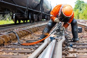 Person with helmet and protective gear working on railroad tracks.