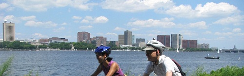 two people riding bikes along a river's edge on a bike path
