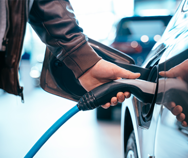 Human hand is holding Electric Car Charging connect to Electric car