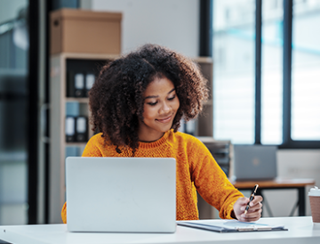 Woman on laptop writing in a notebook