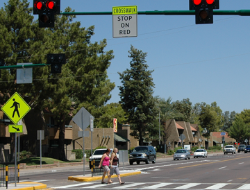 Two women walk in a marked crosswalk across a multi-lane road.