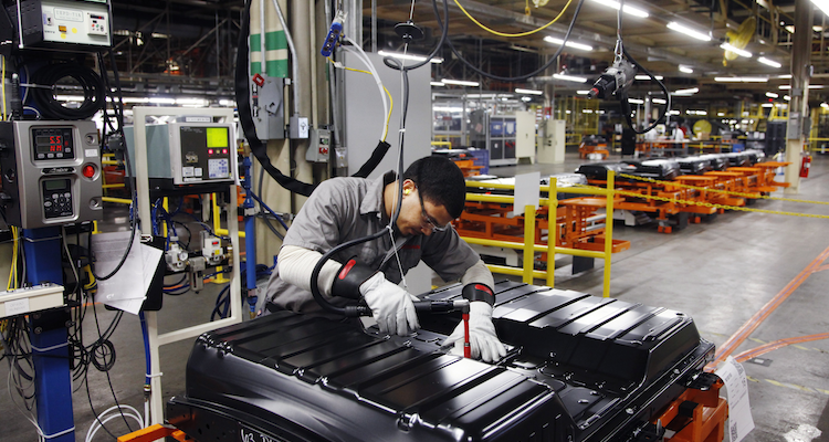A technician assembles part of a vehicle in a manufacturing warehouse.